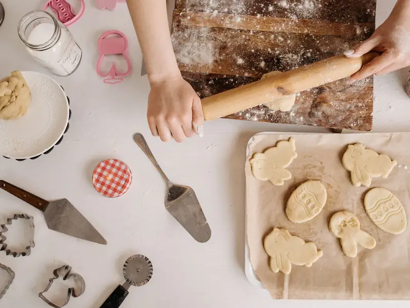 Hands rolling cookie dough beside cutters and baking tools.