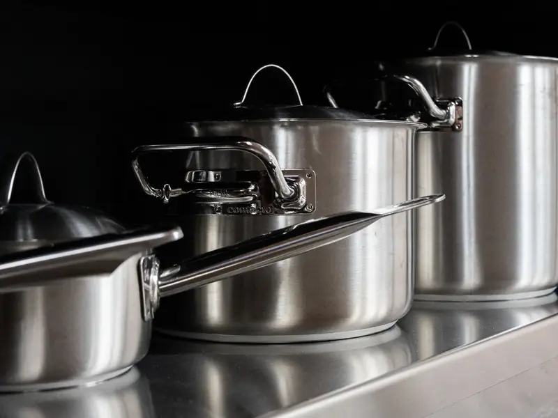Stainless steel cooking pots lined up on a kitchen counter.