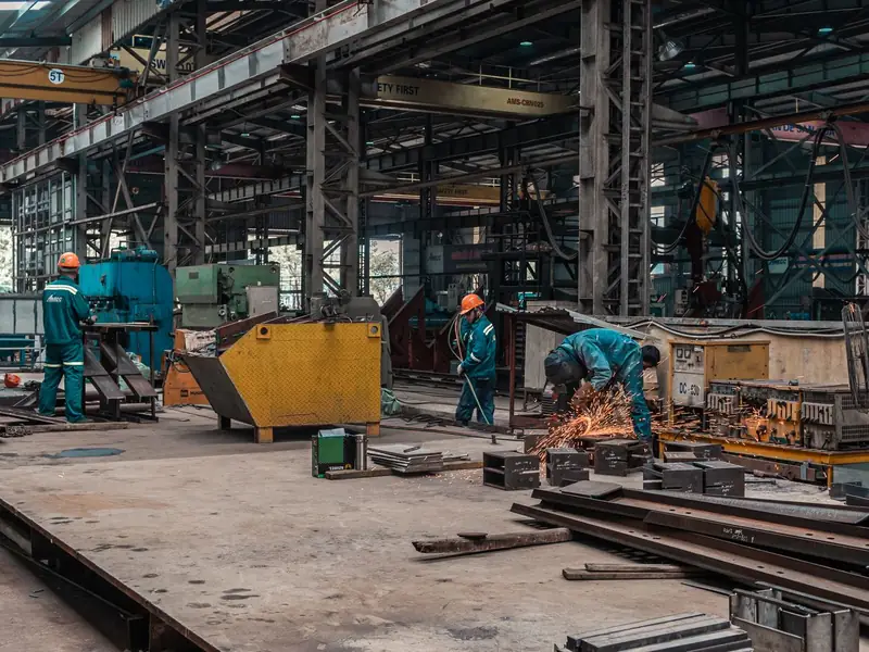Workers and metalworking equipment inside a large industrial workshop.