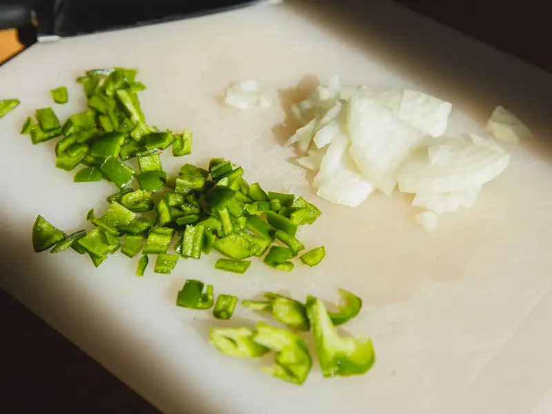 Chopped green pepper and onion beside a knife on a cutting board.